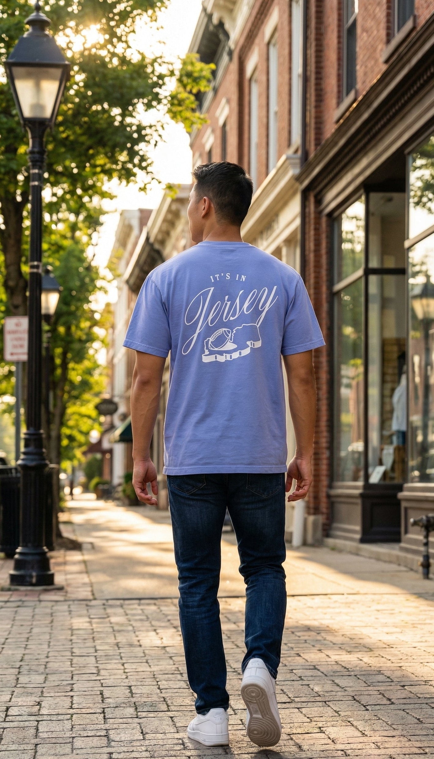 Man walking down a street wearing a blue t-shirt with 'It's a Jersey' text and the state outline with a football